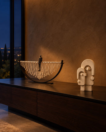 Crescent loop sculpture and double face sandstone sculpture on a dark shelf at night