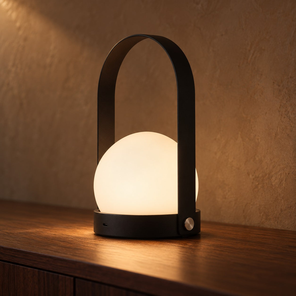 Bue portable table lamp in black with a glowing opal globe on a walnut sideboard