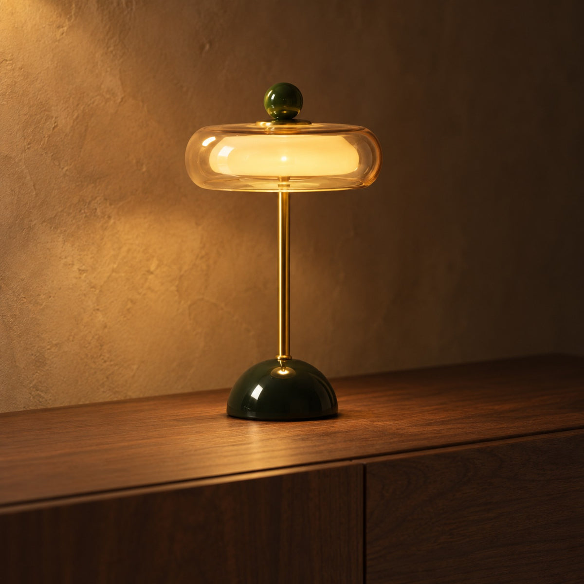 Dark green and brass glass disc lamp glowing on a walnut sideboard