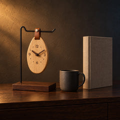 Pebble Hanging Wood Clock beside a coffee mug and a hardcover book, showing its 28 cm height