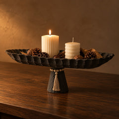 Black pedestal tray with candles and pinecones on a walnut table