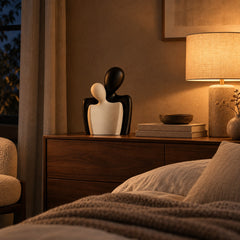 Embrace bust sculptures on a walnut bedroom sideboard at night